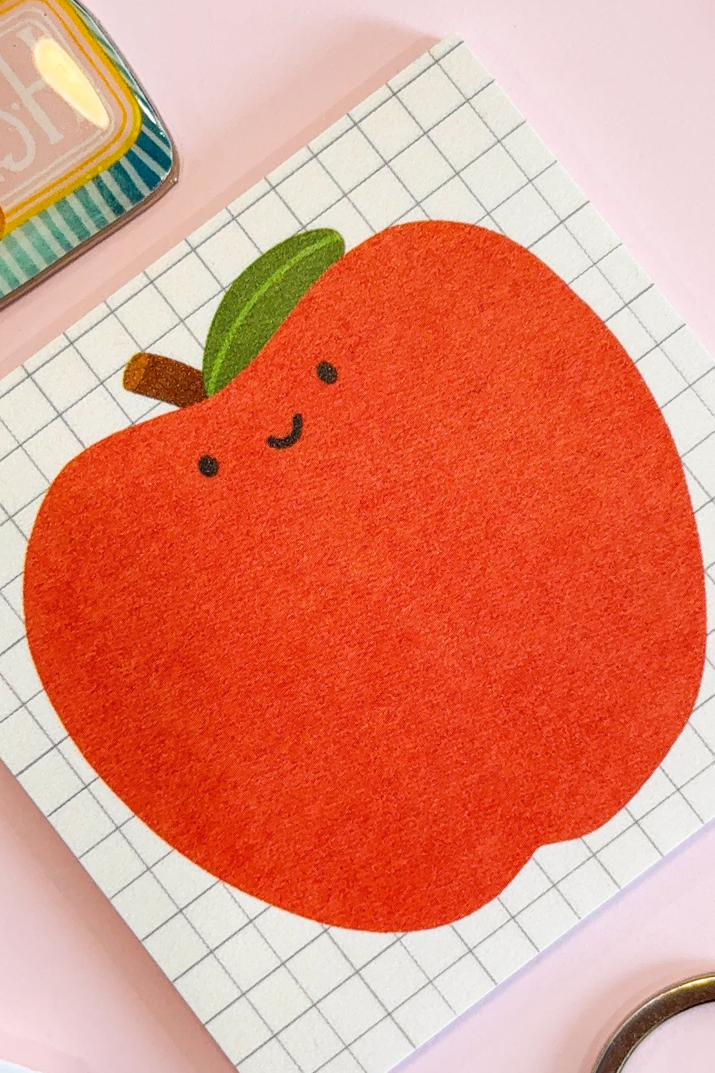 A close-up of an illustrated sticky note featuring a happy illustrated apple on a grid background.