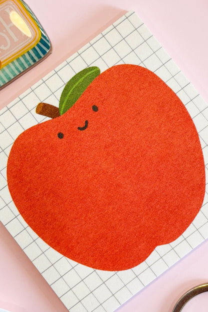 A close-up of an illustrated sticky note featuring a happy illustrated apple on a grid background.